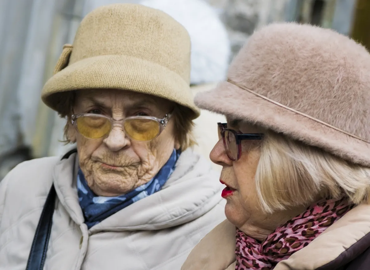 Two older women in soft hats talking face to face